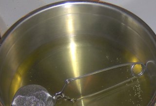 Casserole with tea strainer immersed in a light green liquid